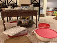 Wicker table with tea set items including teapot, cups, saucers, bowls, and covered plastic storage containers on and around it.