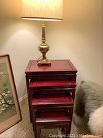 Four nested Asian style dark reddish wooden end tables with carved fretwork, shown with a brass table lamp on top.