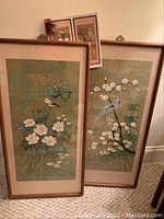 Two framed watercolor paintings leaning against wall on carpet
