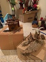 Photo shows a German cuckoo clock with a damaged top piece next to a seashore-themed driftwood sculpture with nautical decorations.