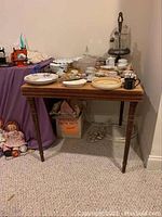Full view of vintage wooden card table holding various dishes and cups, showing overall table shape and condition