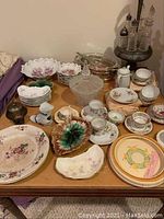 Full view of the table with assorted German china plates, bowls, cups, decorative dishes, and a vintage hotel desk bell.