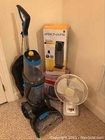 Photo showing Bissell carpet cleaner with blue and gray body, ceramic heater box behind humidifier and white table fan in front.