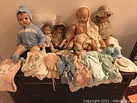 Overview of the collection showing vintage dolls seated behind assorted doll clothing and the musical bells.