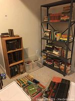 Overview of wooden bookshelf, metal shelving unit and floor stacks of books