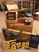 Overall view of stacked boxes and model building showing Athearn, Atlas and Trainpack boxes with small green-roofed building