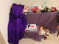 Full lot showing purple gown, linens, dolls, and sewing machines on purple cloth-covered tables.