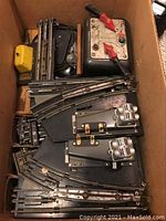 Box containing various track pieces, transformer, and switch controller with red toggles.