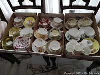 All 16 cups and saucers displayed in three cardboard boxes showing varied designs and colors
