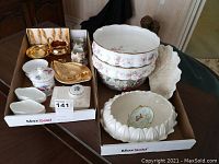 Full view of two trays containing assorted china including white scalloped bowls with pink floral pattern, gold accented small dishes, and covered dishes.