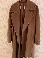 Front view of camel colored Max Mara long coat hanging on wooden wall