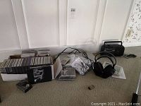 Lot of electronics and media items including Toshiba DVD player, Sony headphones with cables and manual, a portable cassette player, digital clock, multiple CDs and cassette tapes.