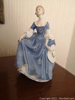 Front view showing the woman in a blue dress with white star patterns and holding a large white hat.