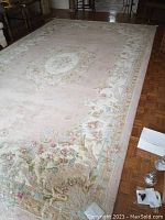 Full view of the coral pink and off white area rug laid out on wooden parquet floor with visible central medallion and floral border pattern.