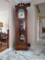 Full front view of clock showing oak-finish wooden case, glass door, base and pediment.