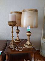 Photo showing the pair of resin lamps with cream lampshades and the tall brass candlestick on a wooden table.