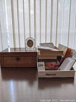 Photo showing the inlay box, stationary items in MaxSold box, and Concept glass clock on a wooden tabletop against a vertical blinds background.