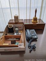 Overview photo of the lot showing wooden boxes, brass bell, quartz clock, Bell Canada phone, and small office accessories arranged on a table.