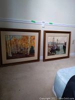 Photo showing both paintings side by side, framed and matted, leaning against a wall on carpeted floor