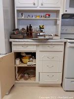 Wide view of kitchen cabinet open showing countertop and shelf with various kitchen baking supplies, knives, and utensils.