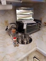 Kitchen counter showing the toaster oven, kettle, spice shakers, glass cup set on tray, and paper towel holder mounted on wall.