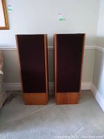 Pair of Realistic Optimus T-100 floor speakers shown side-by-side on carpet, with fabric grilles covering the front faces of the wooden cabinets.