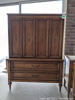 Front view showing four-panel doors, two lower drawers, turned legs and brass-tone handles