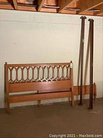 Wooden headboard with carved open oval pattern, matching footboard, and two metal side rails leaning against a beige wall in a basement or garage setting.