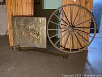 Full lot view showing wooden wagon wheel, embossed brass fire screen, and metal fire tool on floor against wood panel background