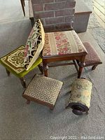 Photo showing various footstools including round and flat tops with needlepoint and floral cushions, along with a wooden chair base without a backrest.