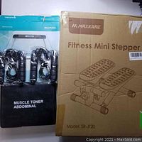 Boxed Maxkare Fitness Mini Stepper SR-JT20 next to black muscle abdominal toner pads.