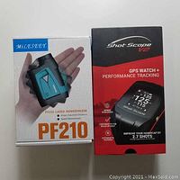 Boxes of MiLESEEY PF210 laser rangefinder and Shot Scope V2 GPS golf watch, showing front with product images and names.