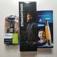 Three boxed grooming items: Philips Norelco Bodygroom Series 1100, Ecardy hair and beard straightener, KM-1910 beard trimmer.