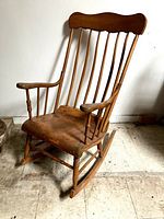 Full front view of the antique wooden rocking chair showing back spindles, armrests, seat, and rockers.