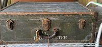 Front view of vintage green trunk with leather handle and key lock, showing wear and patina.