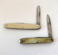 Two vintage pocket knives with blades open, lying flat to show handles and blades