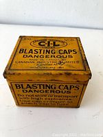 Angle view of yellow vintage metal tin for blasting caps with CIL branding and warning text.
