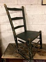 View from angled side showing the full chair structure and rockers, dark paint with significant wear and chipping.