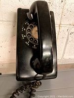 Side view of the black rotary dial phone showing the handset and coiled cord.