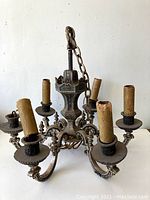 Full view of antique metal chandelier with six damaged faux candle sleeves and ornate metalwork, hanging chain visible.
