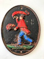 Front view of the oval cast iron fire department sign showing the full fireman figure blowing a horn and holding a torch with flames, painted in red, blue, green, and brown on black background with visible wear.