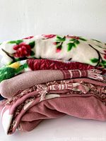 Stack of five folded throw blankets showing various colors and textures including floral fleece and woven fabrics.