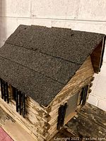 Front and roof view of wooden log cabin style bird house showing textured walls and black shutters