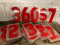 Photo of multiple red acrylic numbers and symbols on clear backing leaning against white wall and stacked on surface.