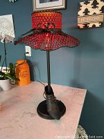 Side view showing red beaded hat-shaped lamp shade, black bow detail, black stem, and black metal shoe base.