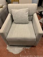 Front view of grey upholstered armchair with toss cushion placed against backrest