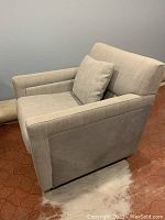 Three-quarter view of the grey fabric arm chair with toss cushion and solid wood base