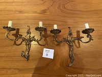 Pair of ornate brass French antique wall sconces on wood surface, showing front and detail with faux candle bulbs.