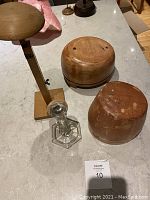 Two round wooden hat molds, adjustable wooden stand, and glass stand on countertop