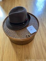 Brown vintage fur felt men's hat resting on a woven bamboo round hat box with cuff links beside it